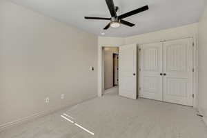 Unfurnished bedroom with light colored carpet, a ceiling fan, and a closet