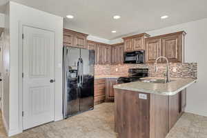 Kitchen with black appliances, a peninsula, tasteful backsplash, recessed lighting, and light countertops