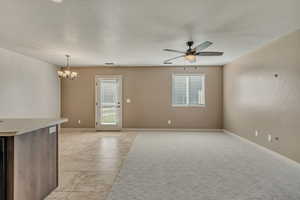 Unfurnished living room featuring plenty of natural light, light tile patterned floors, a chandelier, and a ceiling fan