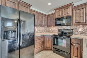 Kitchen with black appliances, light tile patterned flooring, backsplash, brown cabinetry, and recessed lighting