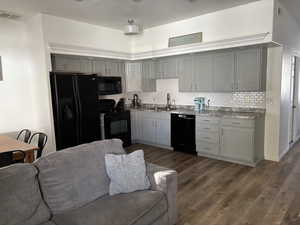 Kitchen featuring gray cabinets, black appliances, decorative tile backsplash, wood style LVP flooring, and light counters
