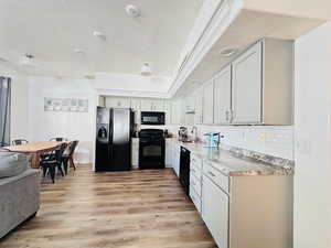 Kitchen with light countertops, tasteful backsplash, light wood LVP floors, black appliances, and white cabinets