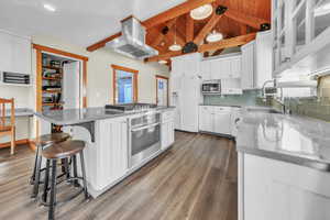Kitchen featuring white cabinets, tasteful backsplash, light stone counters, island range hood, and appliances with stainless steel finishes