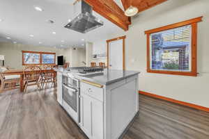 Kitchen featuring island range hood, beamed ceiling, stainless steel appliances, a center island, and white cabinets