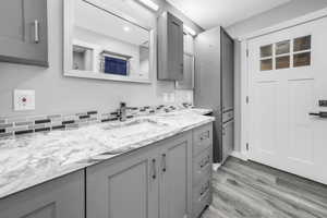 Kitchen with gray cabinetry, decorative backsplash, light wood-type flooring, and light stone countertops