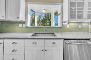 Kitchen with dishwasher, white cabinets, dark stone counters, and tasteful backsplash