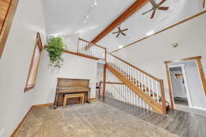 Stairs with beam ceiling, high vaulted ceiling, ceiling fan, and carpet