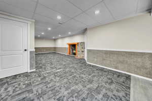 Finished below grade area featuring a paneled ceiling, carpet floors, recessed lighting, and wainscoting