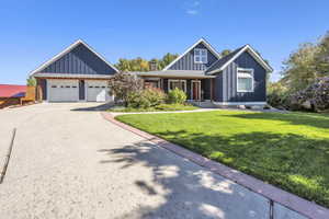 View of front of house featuring board and batten siding, covered porch, driveway, a front yard, and a garage