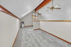 Additional living space featuring light carpet, a skylight, and a ceiling fan