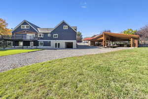 Rear view of house featuring a lawn, a deck, board and batten siding, gravel driveway, and roof with shingles
