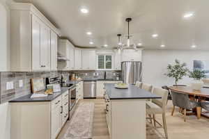 Kitchen with dark countertops, a breakfast bar area, appliances with stainless steel finishes, tasteful backsplash, and hanging light fixtures