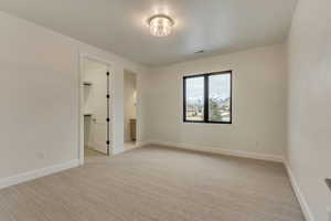 Unfurnished bedroom featuring light colored carpet, a walk in closet, and ensuite bath