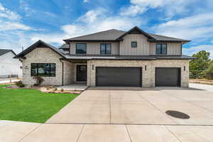 Modern farmhouse with a standing seam roof, a metal roof, an attached garage, concrete driveway, and stone siding