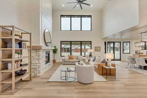 Living area featuring recessed lighting, a stone fireplace, light wood finished floors, a towering ceiling, and ceiling fan