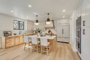 Kitchen featuring a breakfast bar, pendant lighting, an island with sink, light wood-style floors, and recessed lighting
