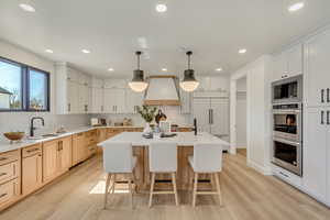 Kitchen with decorative light fixtures, a breakfast bar, a center island with sink, built in appliances, and light wood-style floors