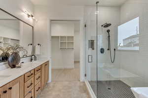 Full bath with a spacious closet, double vanity, a stall shower, and light tile patterned floors