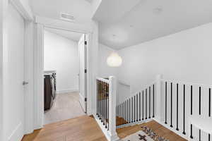Corridor featuring an upstairs landing, light wood finished floors, and washing machine and dryer