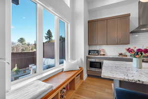 Kitchen with light stone counters, wall chimney range hood, decorative backsplash, light wood-type flooring, and stainless steel microwave