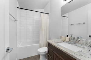 Bathroom featuring shower / bath combination with curtain, vanity, and dark wood-style floors