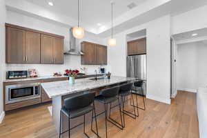 Kitchen featuring light stone counters, stainless steel appliances, an island with sink, a kitchen bar, and hanging light fixtures