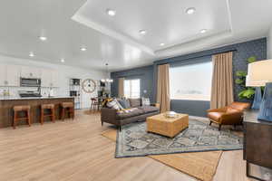 Living area featuring a raised ceiling, wallpapered walls, light wood-type flooring, recessed lighting, and a chandelier