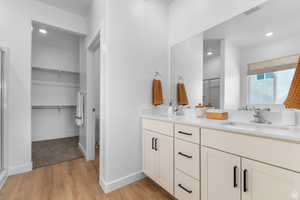 Bathroom with light wood-style flooring, a shower stall, a spacious closet, double vanity, and recessed lighting