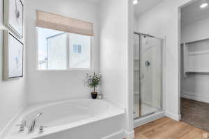 Bathroom with a spacious closet, a stall shower, light wood-style flooring, and a bath