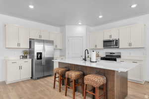 Kitchen featuring appliances with stainless steel finishes, light wood-style flooring, a center island with sink, a kitchen bar, and recessed lighting