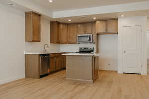Kitchen with recessed lighting, appliances with stainless steel finishes, brown cabinets, a kitchen island, and light wood-style floors