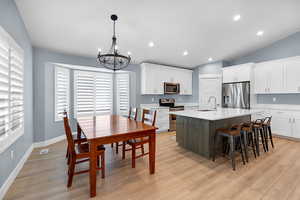 Kitchen featuring white cabinets, appliances with stainless steel finishes, an island with sink, recessed lighting, and vaulted ceiling