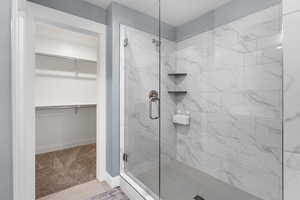 Full bath featuring a spacious closet, a marble finish shower, light carpet, and light tile patterned flooring
