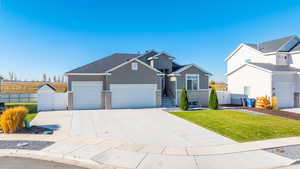 View of front facade featuring stucco siding, driveway, stone siding, a garage, and a gate