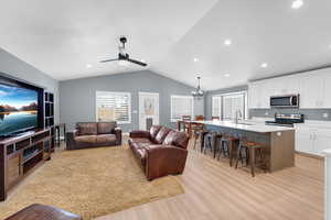 Living room with a chandelier, a ceiling fan, vaulted ceiling, light wood-style flooring, and recessed lighting