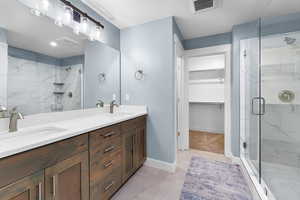 Full bathroom featuring a walk in closet, double vanity, light tile patterned floors, and a shower stall