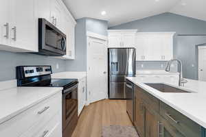 Kitchen with stainless steel appliances, white cabinets, light wood finished floors, light stone counters, and lofted ceiling