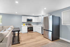 Kitchen with stainless steel appliances, open floor plan, white cabinetry, light wood finished floors, and recessed lighting