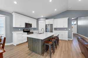 Kitchen featuring stainless steel appliances, white cabinetry, a center island with sink, a kitchen bar, and light wood finished floors