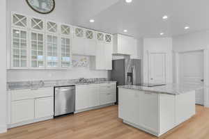 Kitchen featuring light stone countertops, glass insert cabinets, white cabinets, dishwasher, and recessed lighting. Laudry to right of pantry