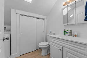 ADU bathroom with light wood-type flooring, washer / dryer, vanity, a skylight, and vaulted ceiling with storage/linen closet