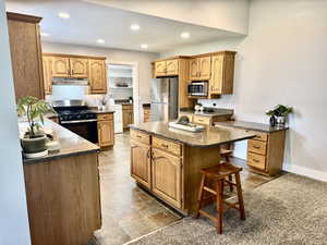 Kitchen featuring appliances with stainless steel finishes, a kitchen island, recessed lighting, dark stone countertops, and under cabinet range hood