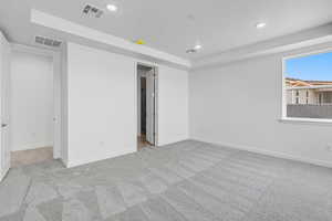 Unfurnished bedroom with light carpet, recessed lighting, and a raised ceiling