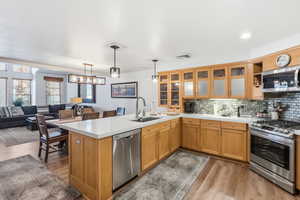 Kitchen with appliances with stainless steel finishes, decorative backsplash, light wood finished floors, and hanging light fixtures