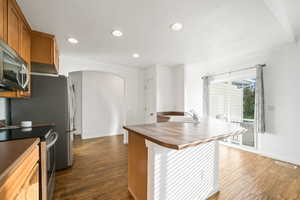 Kitchen with appliances with stainless steel finishes, arched walkways, brown cabinets, recessed lighting, and dark wood-type flooring
