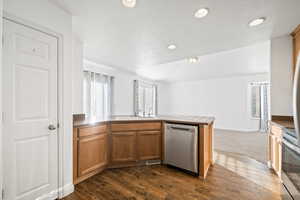 Kitchen with appliances with stainless steel finishes, brown cabinets, dark wood finished floors, a textured ceiling, and a peninsula