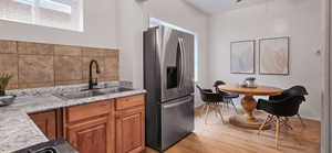 Kitchen with stainless steel refrigerator with ice dispenser, brown cabinetry, light countertops, light wood-style floors, and tasteful backsplash