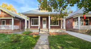 Bungalow-style house with a front lawn, a porch, roof with shingles, and brick siding