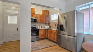 Kitchen with stainless steel appliances, brown cabinetry, light wood-type flooring, light stone countertops, and tasteful backsplash