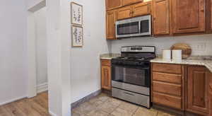 Kitchen featuring appliances with stainless steel finishes, brown cabinetry, light stone countertops, and light wood-type flooring